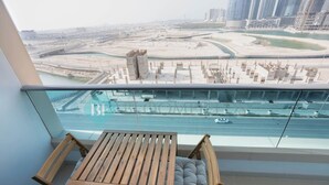A balcony with a wooden table and chairs, offering a view of a cityscape with buildings and a waterway. - Bloomfields Premium STU Canal View Julphar Tower (Abu Dabi)