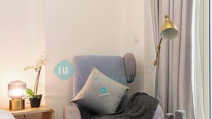 A cozy room with a grey armchair, a small wooden side table with a lamp, a potted orchid, and a grey blanket. - Bloomfields STU Farishta Alfurjan near Metro (Dubai)