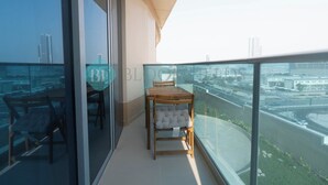 Uma varanda com guarda-corpo de vidro, mesa de madeira e cadeira estofada.