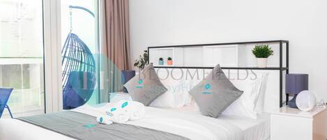 Une chambre d’hôtel moderne, équipée d’un lit, d’une table de chevet avec une lampe, d’une chaise et d’une fenêtre avec des rideaux.