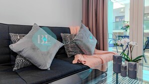 Un salon moderne avec un canapé foncé, des coussins à motifs, un plaid tricoté et des vases décoratifs.