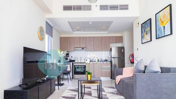 Uma sala de estar moderna com um sofá cinza, um móvel de entretenimento preto e uma cozinha ao fundo.