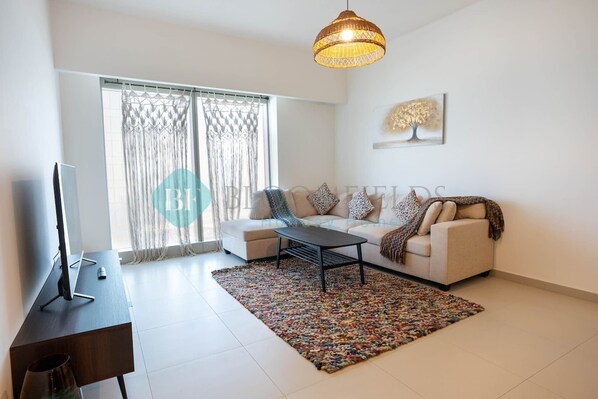 A modern living room with a sofa, coffee table, and a TV on a desk. - Bloomfields Cozy 1BR in Gate Tower Al Reem (Abu Dabi)