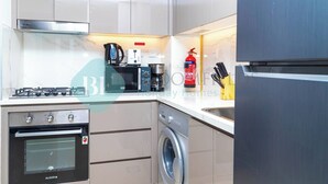 Cozinha compacta com fogão a gás, forno, máquina de lavar e geladeira.