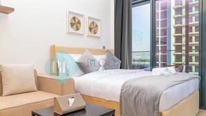 A hotel room with a bed, a sofa, a small table with a laptop, and a window with a view of a building. - Bloomfields STU City View Azizi Riviera Meydan (Dubai)