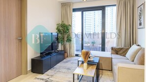 Een moderne woonkamer met een bank, een salontafel, een televisie en een groot raam met gordijnen.