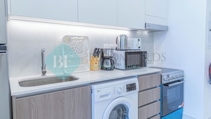 A compact kitchen with a washing machine, microwave, and oven. - Bloomfields Spacious STU in Thalassa Beach Front (Abu Dabi)