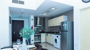 A modern kitchen with stainless steel appliances, a washing machine, and a dining area with a table set for four. - Bloomfields 1BR Ocean View in OceanScape (Abu Dabi)