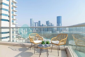 En balkon med to fletstole og et lille bord, med udsigt over en by med moderne bygninger.