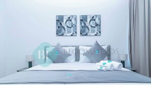 A hotel room with a neatly made bed, two wall-mounted artworks, a lamp, and a folded towel on the bed. - Bloomfields 1BR Ocean View in OceanScape (Abu Dabi)