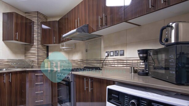 A modern kitchen with wooden cabinets, a built-in oven, a microwave, and a washing machine.