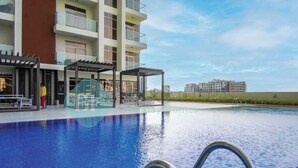 A swimming pool with a clear view of the surrounding buildings and a covered seating area. - Bloomfields Hidden Gem Studio In Arjan (Dubai)