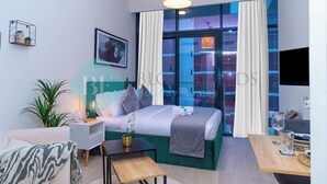 A modern hotel room with a large bed, a desk, a chair, a potted plant, and a view of the cityscape through large windows. - Bloomfields Fantastic STU Azizi Riviera Meydan (Dubai)