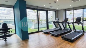 A gym with treadmills, a bench press, and large windows offering a view of the outdoors. - Bloomfields Fantastic STU Azizi Riviera Meydan (Dubai)