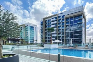 Een modern hotel met een zwembad, meerdere verdiepingen en een heldere lucht.