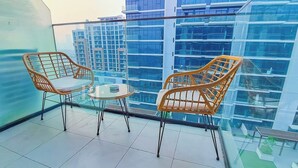 A balcony with two wicker chairs and a small round table, overlooking a cityscape with modern buildings. - Bloomfields Fantastic STU Azizi Riviera Meydan (Dubai)