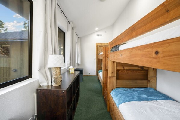 A bunk bed room with a window, a lamp, a dresser, and a green carpet.