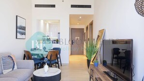 A modern living room with a sofa, a coffee table, a TV, and a dining area with chairs and a table. - Bloomfields Stylish 1BR Binghatti Heights JVC (Dubai)