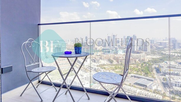 A balcony with two metal chairs and a small round table, overlooking a cityscape. - Bloomfields Stylish 1BR Binghatti Heights JVC (Dubai)