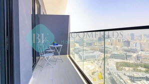 Un balcón con vistas a la ciudad, una pequeña mesa con sillas y una planta en maceta.