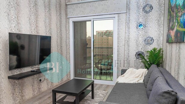 Een moderne woonkamer met een flatscreen televisie, een donkere salontafel, een grijze bank en een schuifpui naar een buitenruimte.