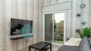 Een moderne woonkamer met een flatscreen televisie aan een gestructureerde muur, een donkere salontafel, een grijze bank en een glazen schuifdeur naar een buitenruimte.