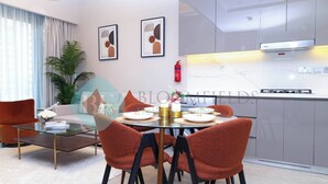 Un espace repas moderne avec une table en verre, des chaises à revêtement rouge et une cuisine en arrière-plan.
