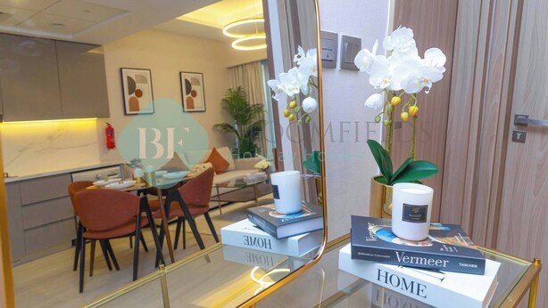 Une chambre d’hôtel moderne avec un coin repas, un miroir qui reflète la pièce et un vase rempli de fleurs blanches.