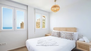 Ein Schlafzimmer mit einem Bett, zwei Nachttischen, einem Beistelltisch, einem Rattan-Kopfende und einer Pendelleuchte.