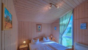 A wooden cabin bedroom with a single bed, bedside tables, and a window with curtains. - Skandinavisches Ferienhaus in Rechlin (Rechlin)