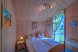 Un dormitorio de cabaña de madera con una cama individual, mesitas de noche y una ventana con cortinas.