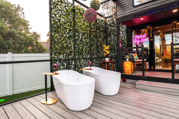An outdoor seating area with white, modern stools and a small round table, surrounded by a lush green wall with hanging plants.