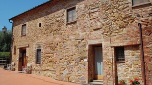 A stone building with multiple windows and doors, a tiled entrance, and outdoor seating. - Comiti Farmhouse - Apt. Sanzio (Montaione)