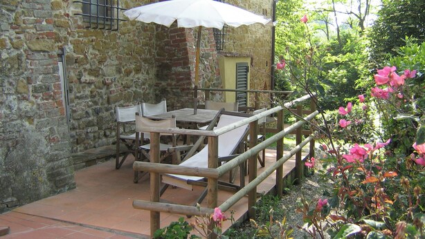 An outdoor patio with a wooden table and chairs, a white umbrella, and a stone building in the background. - Comiti Farmhouse - Apt. Sanzio (Montaione)