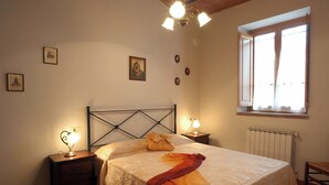 A bedroom with a bed, two bedside tables, a window, and a radiator. - Comiti Farmhouse - Apt. Sanzio (Montaione)