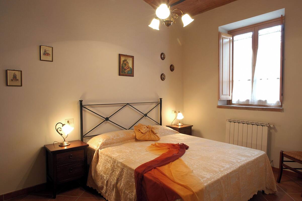 A bedroom with a bed, two bedside tables, a window, and a radiator.