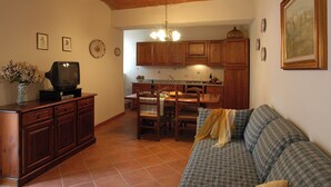 A living room with a sofa, a television, and a dining area with a table and chairs. - Comiti Farmhouse - Apt. Sanzio (Montaione)