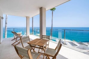Un balcon avec une table et des chaises en bois, donnant sur un océan d’un bleu limpide.