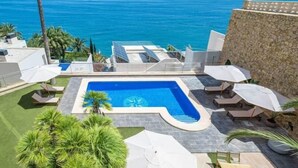 A rooftop pool with a view of the ocean, surrounded by lounge chairs and umbrellas.