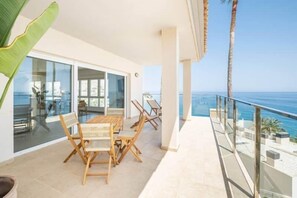 Un balcon avec une table et des chaises, une porte vitrée donnant sur une pièce, et une vue sur la mer.