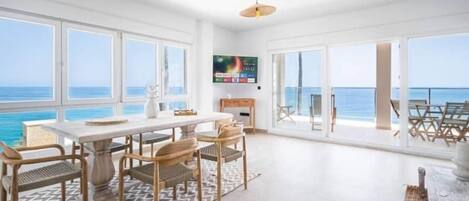 A spacious room with a large table and chairs, a television, and a view of the ocean.