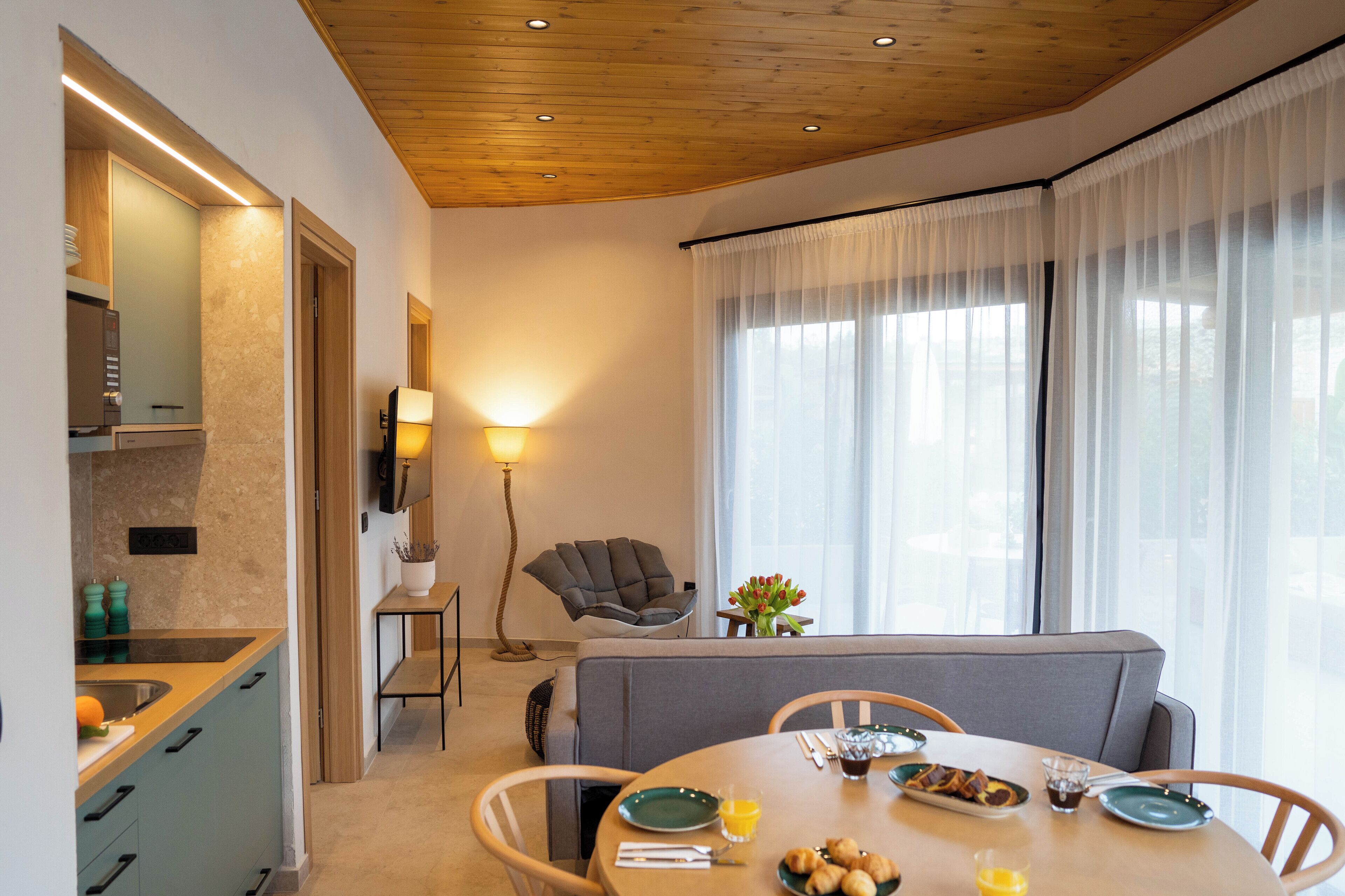 Un espace repas moderne avec une table ronde, des chaises et un canapé. On y trouve également un coin cuisine avec un évier et des placards. Une lampe et une chaise sont également visibles.