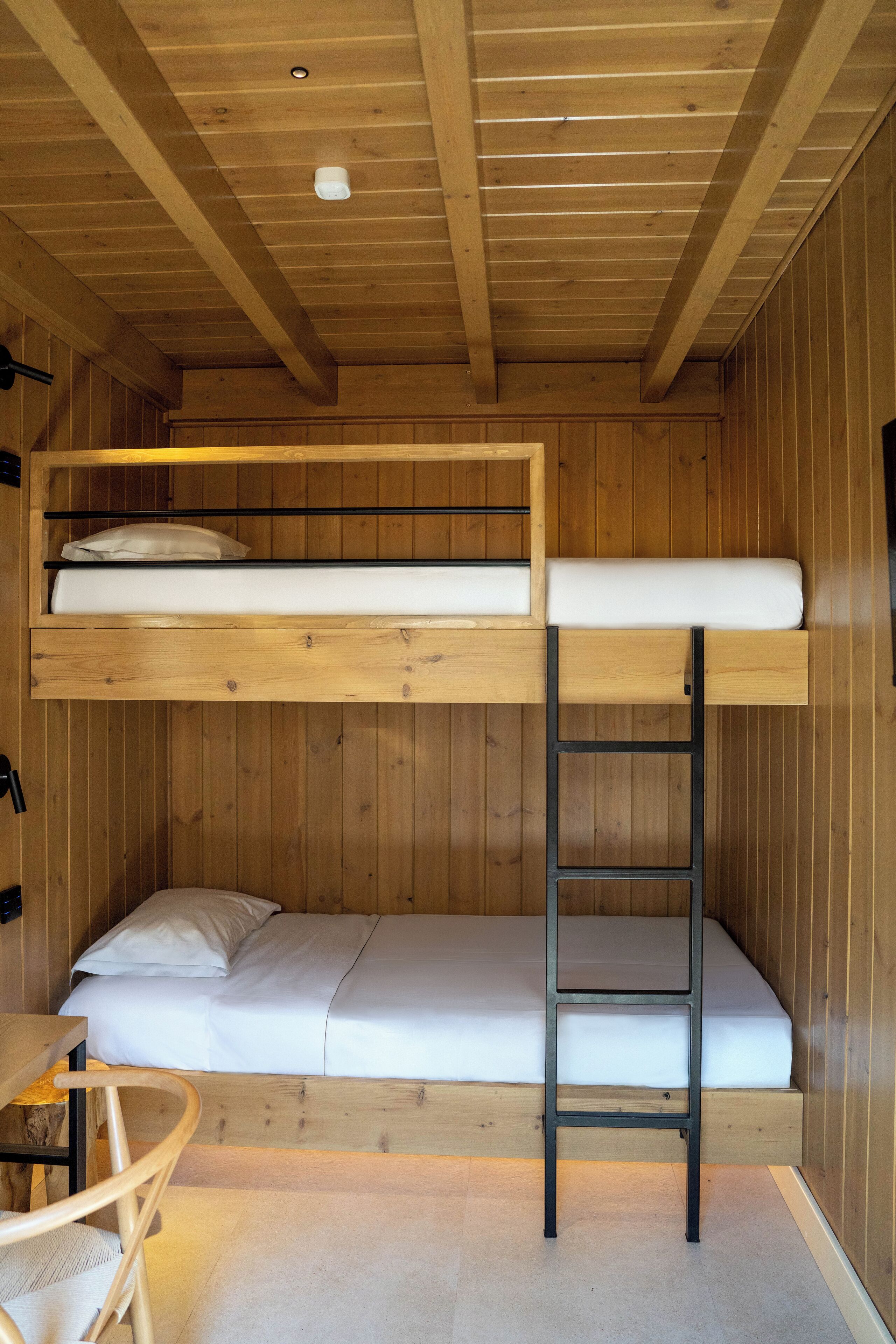 Une chambre avec un lit superposé, une échelle, des murs en bois et une petite table.