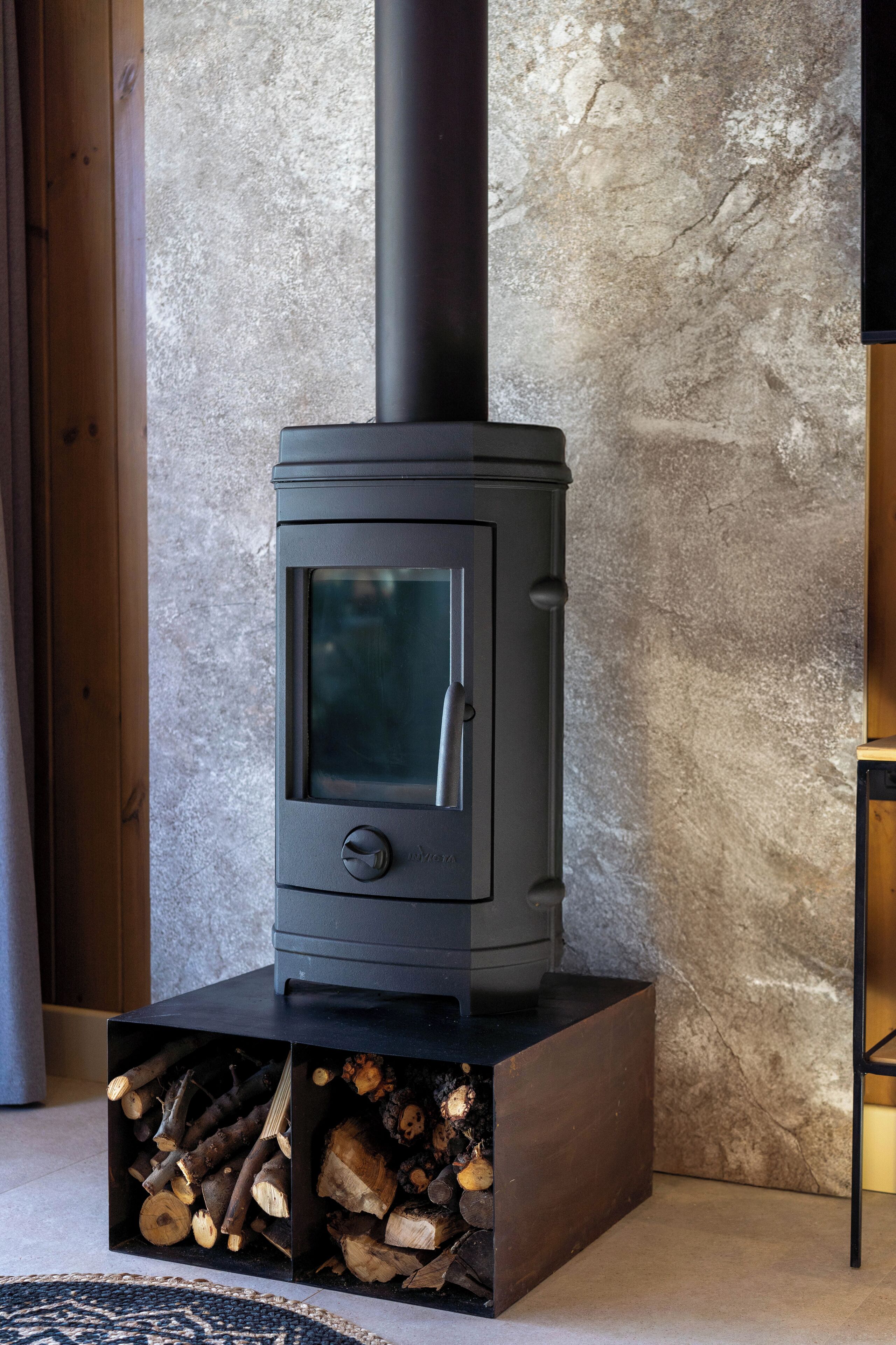 A wood-burning stove with a glass door, placed on a wooden platform with logs.