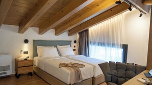 A bedroom with a large bed, a bedside table, a chair, and a window with curtains. - Pure Nature (Hersonissos)