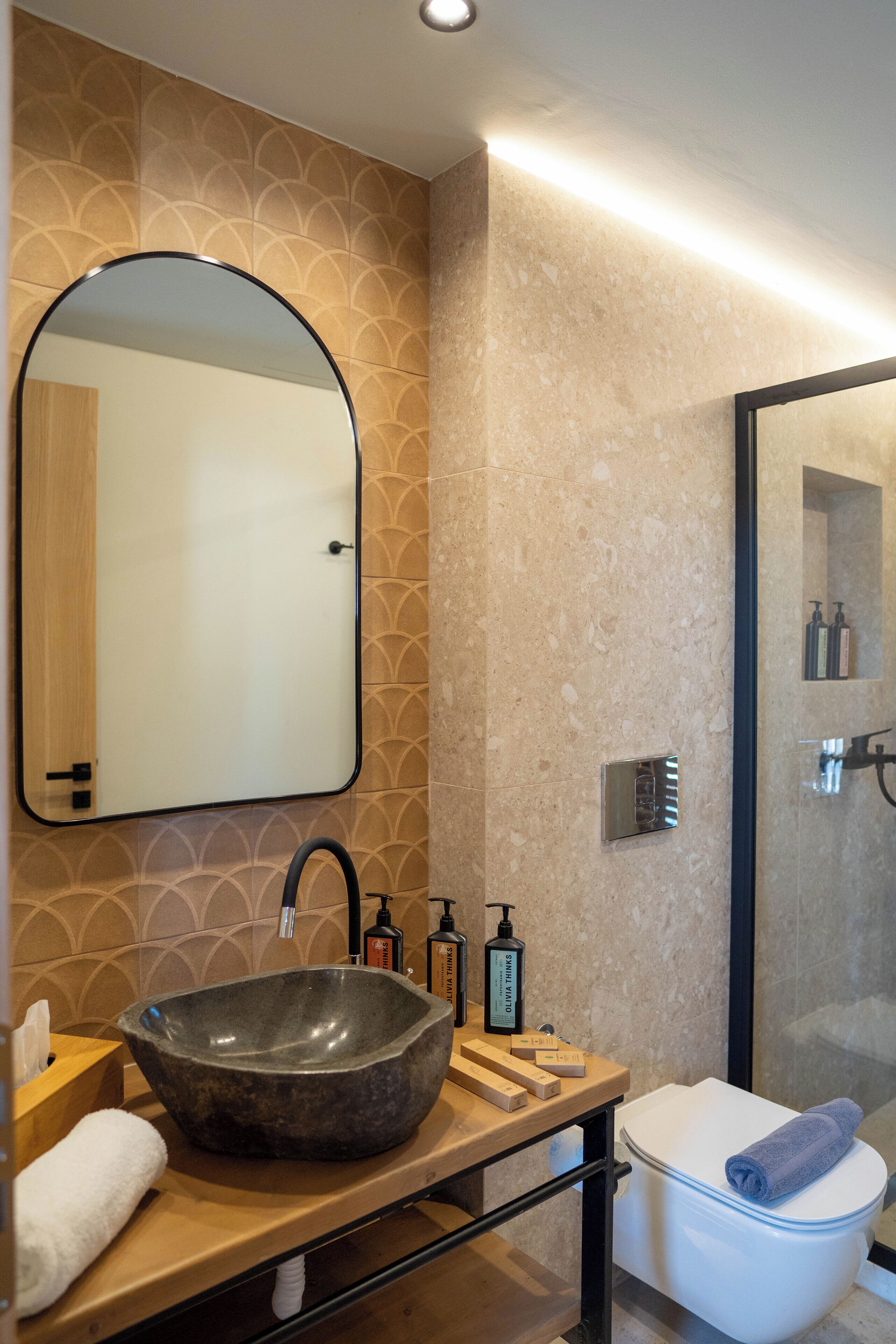 A modern bathroom with a large oval sink, a mirror, a toilet, and a shower area.