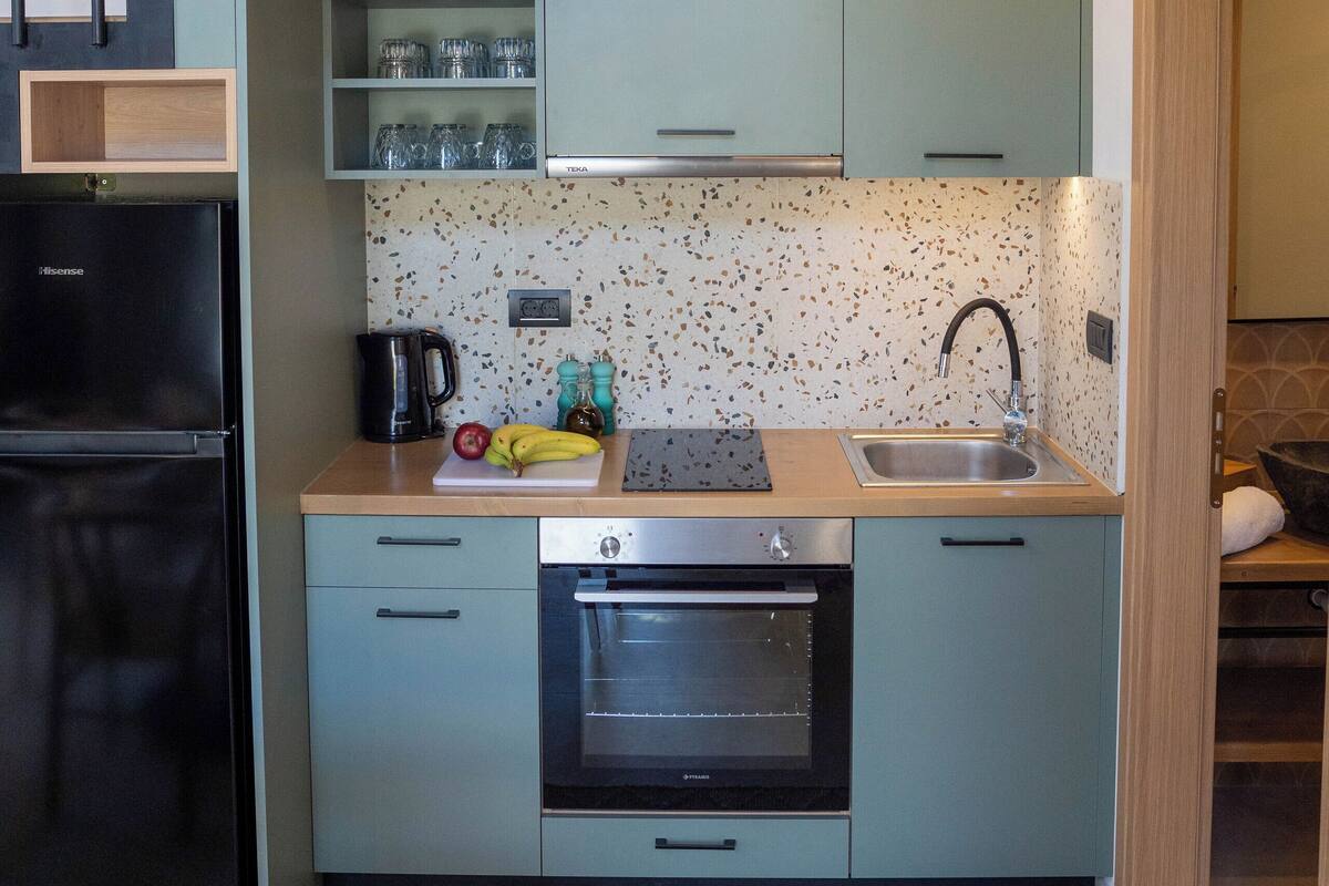 A compact kitchen with a built-in oven, a sink, and a coffee maker. There is a staircase leading to an upper level.