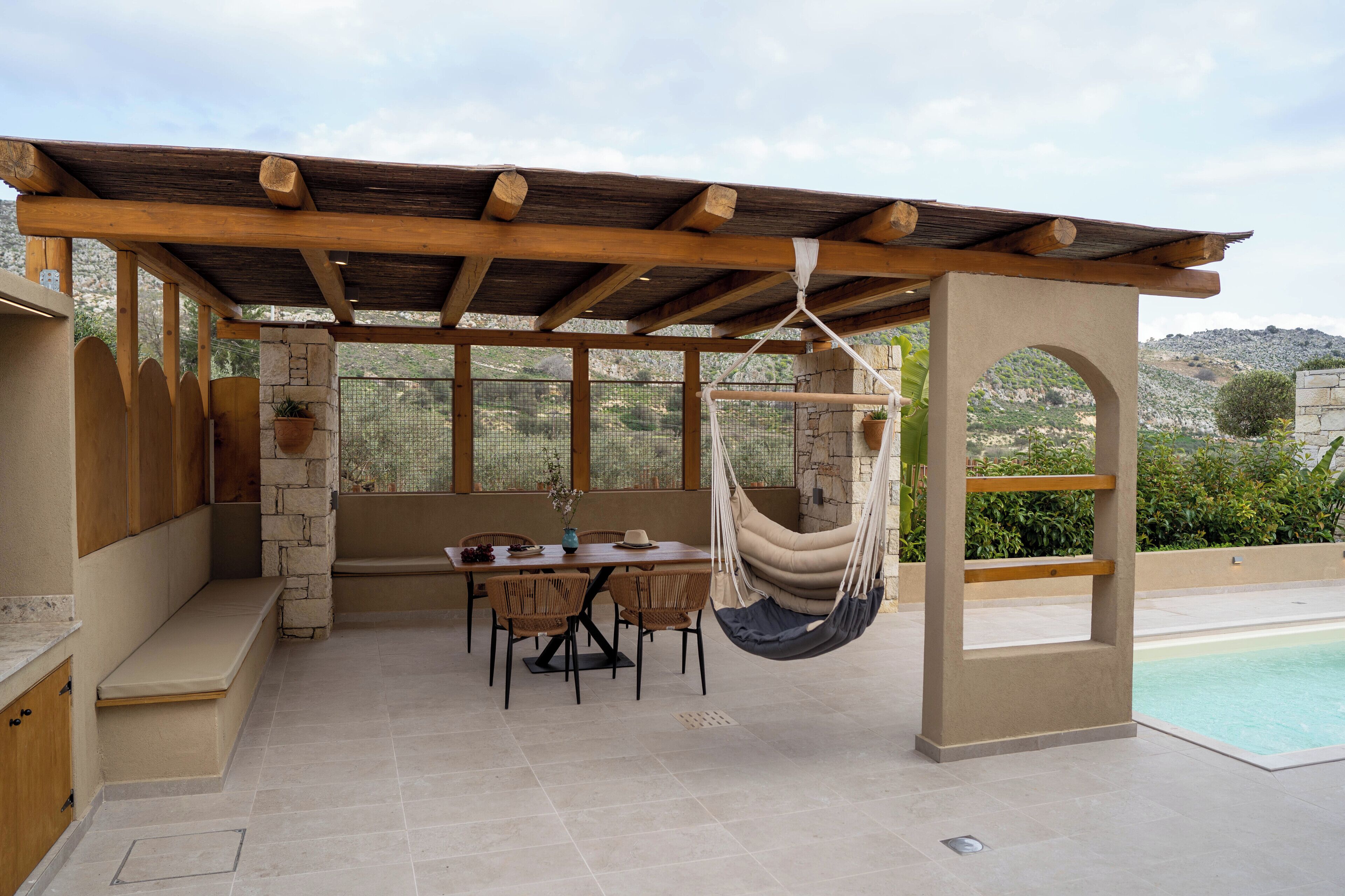 A covered outdoor seating area with a pool, stone walls, and a hanging chair.