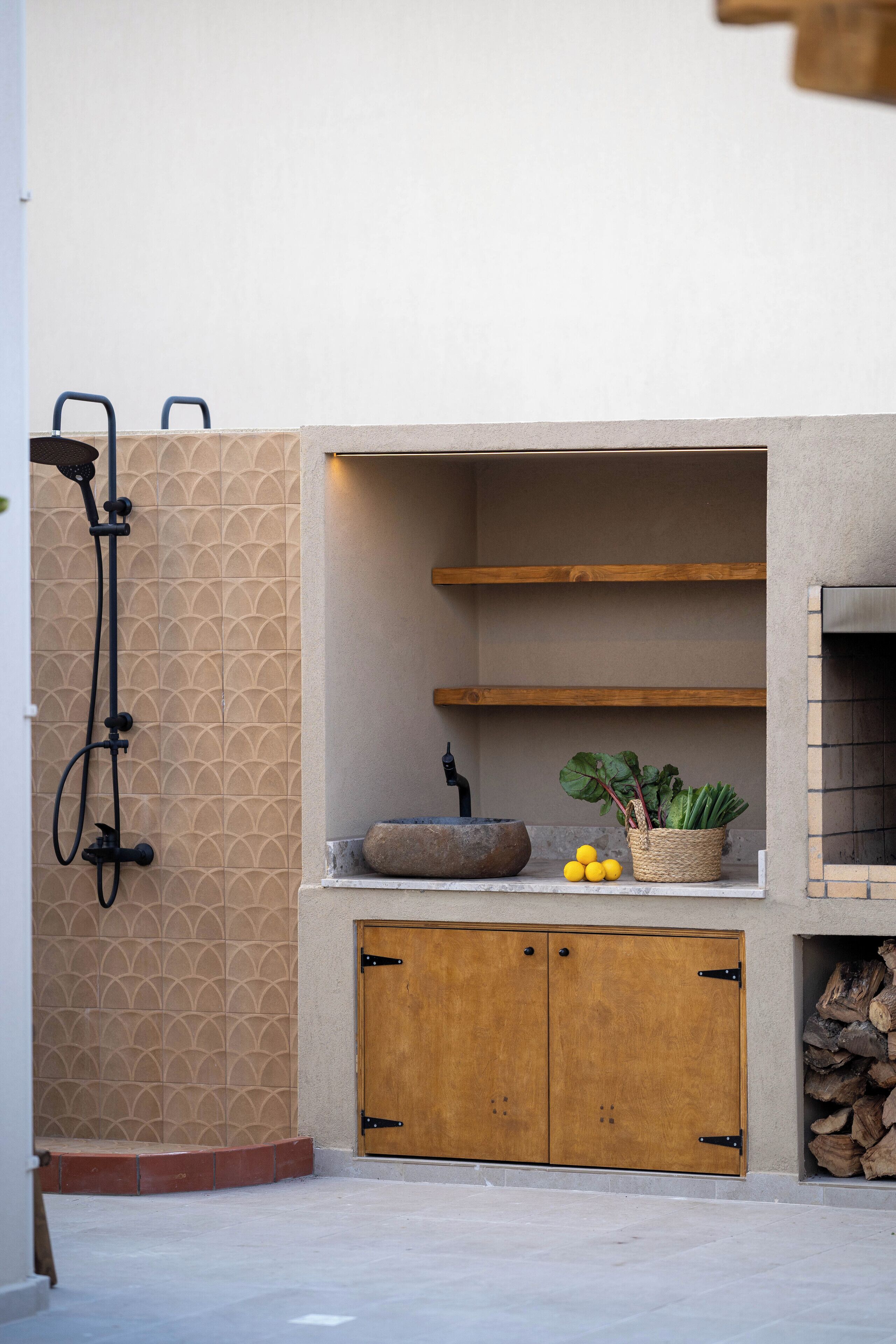 A bathroom with a shower, a sink with a stone basin, wooden cabinets, and a shelf with plants.