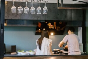 Interior de un restaurante con lámparas colgantes, una barra y vista al área de la cocina.